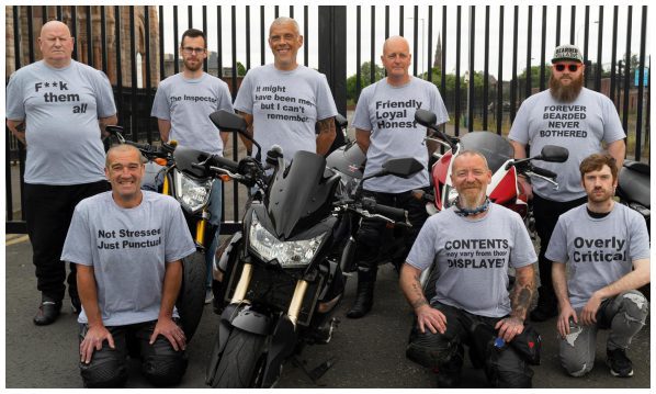 Eight men standing with motorbikes. They're wearing grey T-shirts with phrases that they've chosen themselves to represent themselves and their identity.
